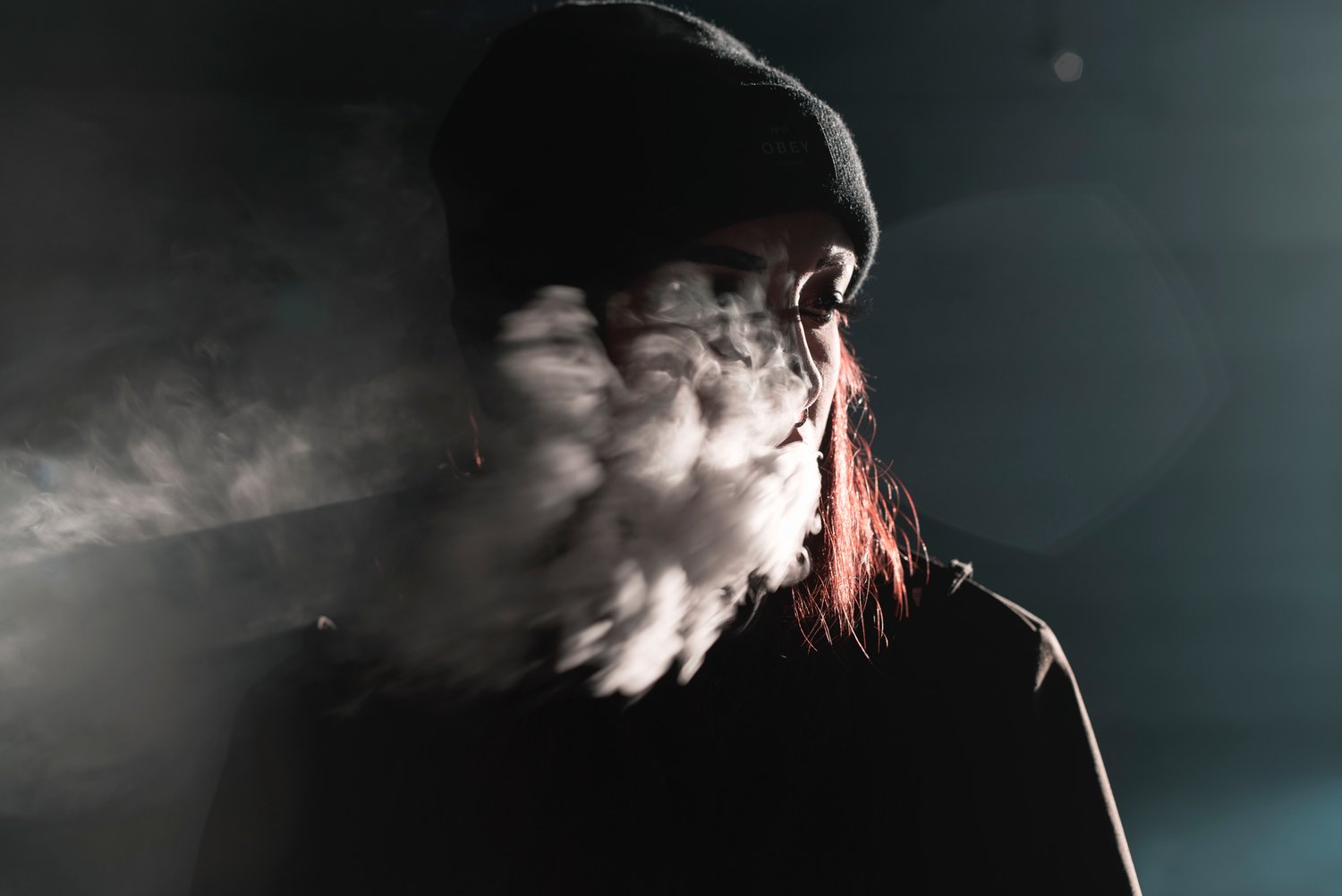 person with smoke in front of her face wearing a hat