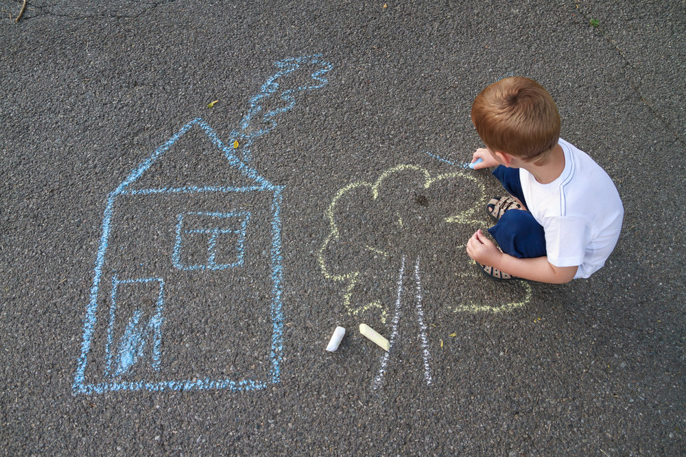 child drawing a house and tree with chalk outside