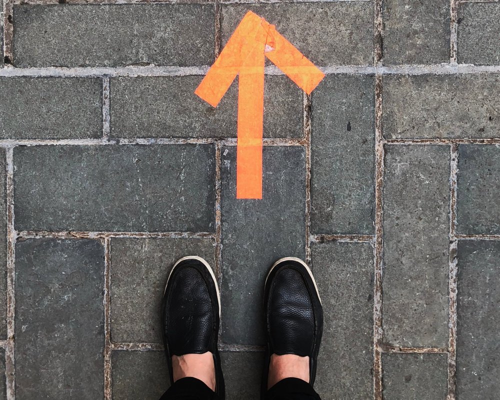 person's feet on a sitewalk with an arrow pointing forward