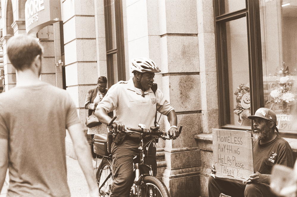 security person on a bike interacting with a homeless person on the sidewalk