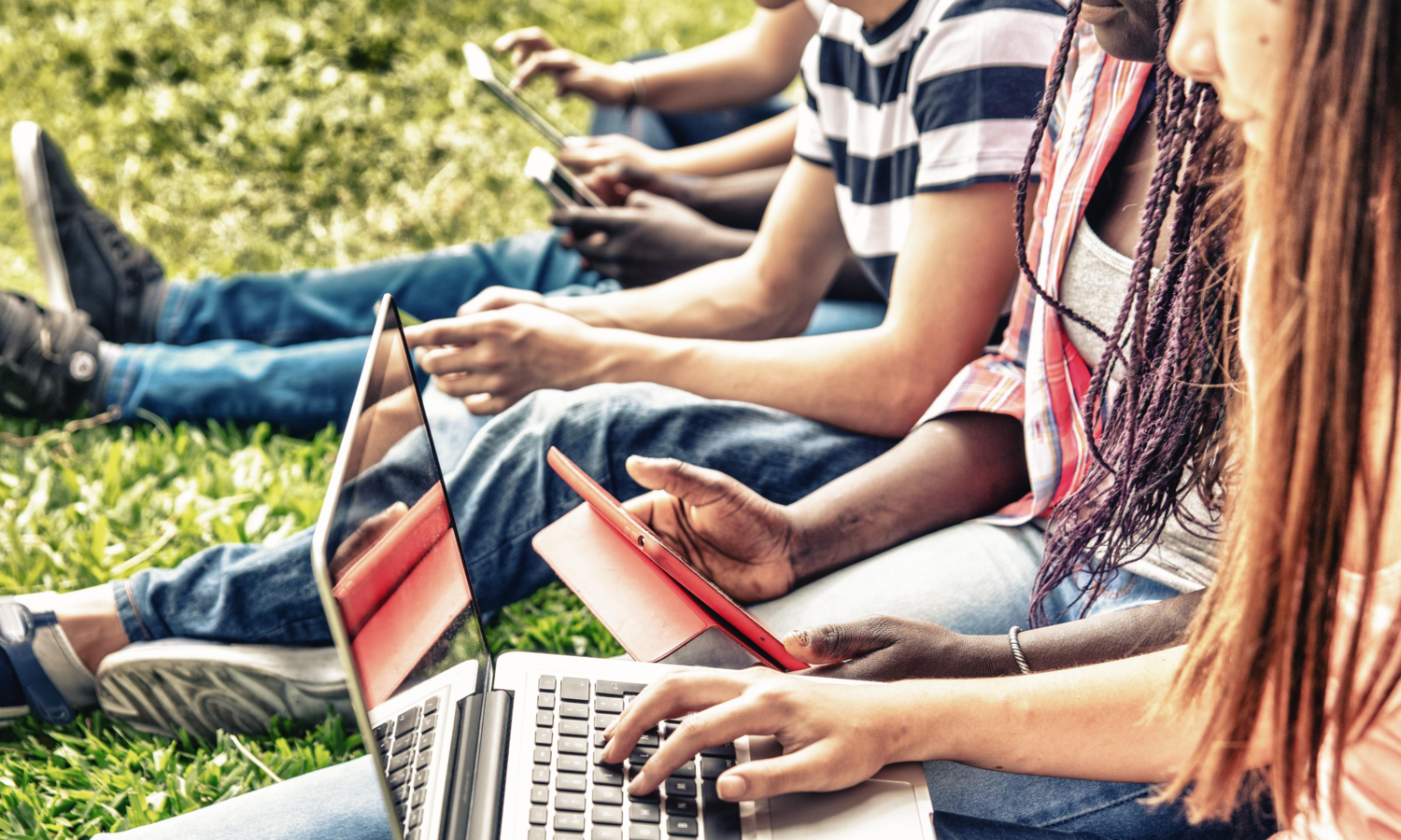 kids sitting in the grass on phones and laptops