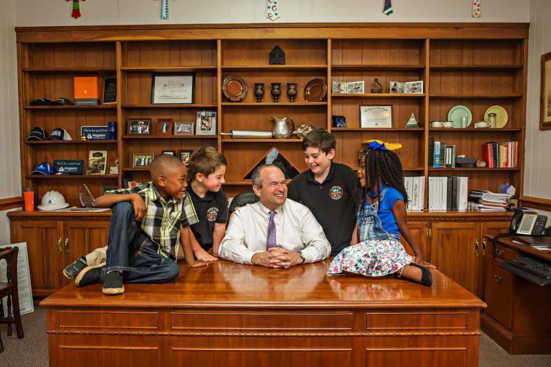 kids around a man at his desk smiling