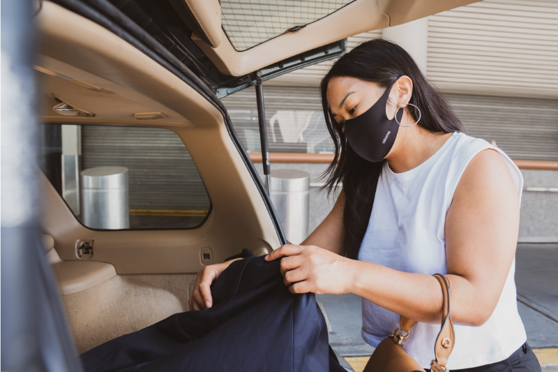 woman wearing facemask and going through gear in the trunk of her car