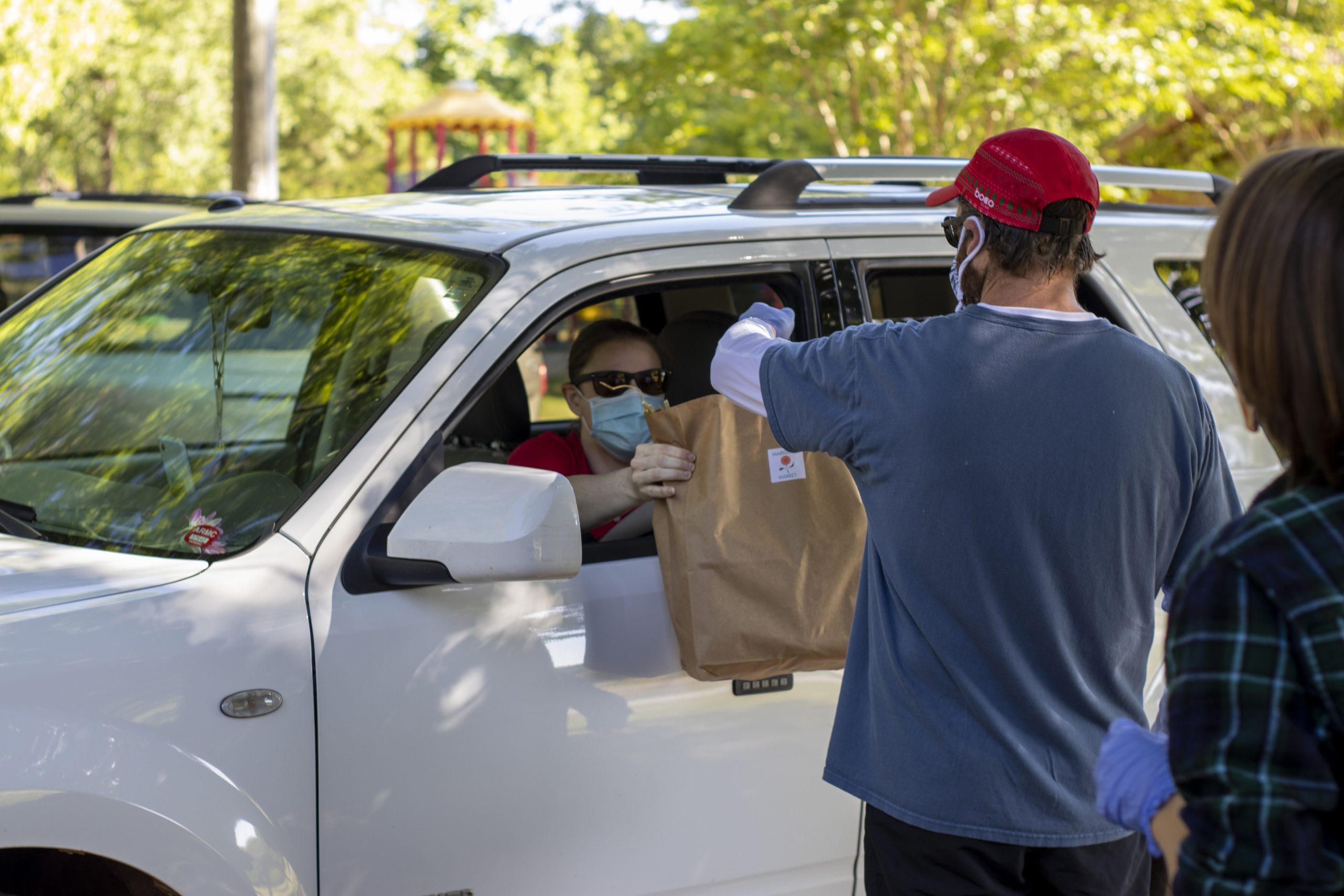 A volunteer wearing protective mask and gloves distributes a pre-paid order to a drive-up customer