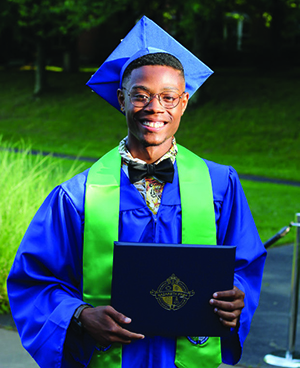 student smiling and holding diplona in cap and gown