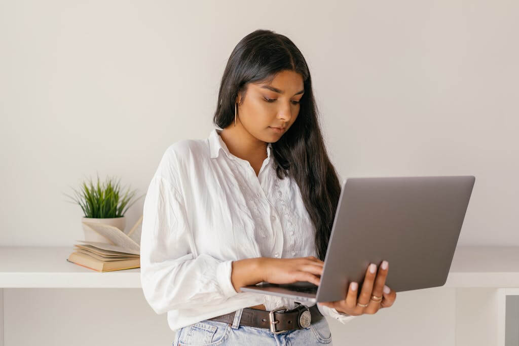 A young woman typing on a laptop while standing indoors, focused and professional.